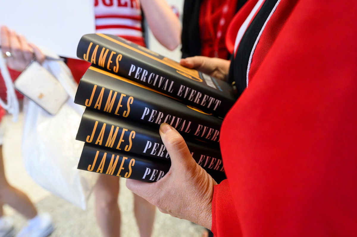 A person in red academic robes hands out books.