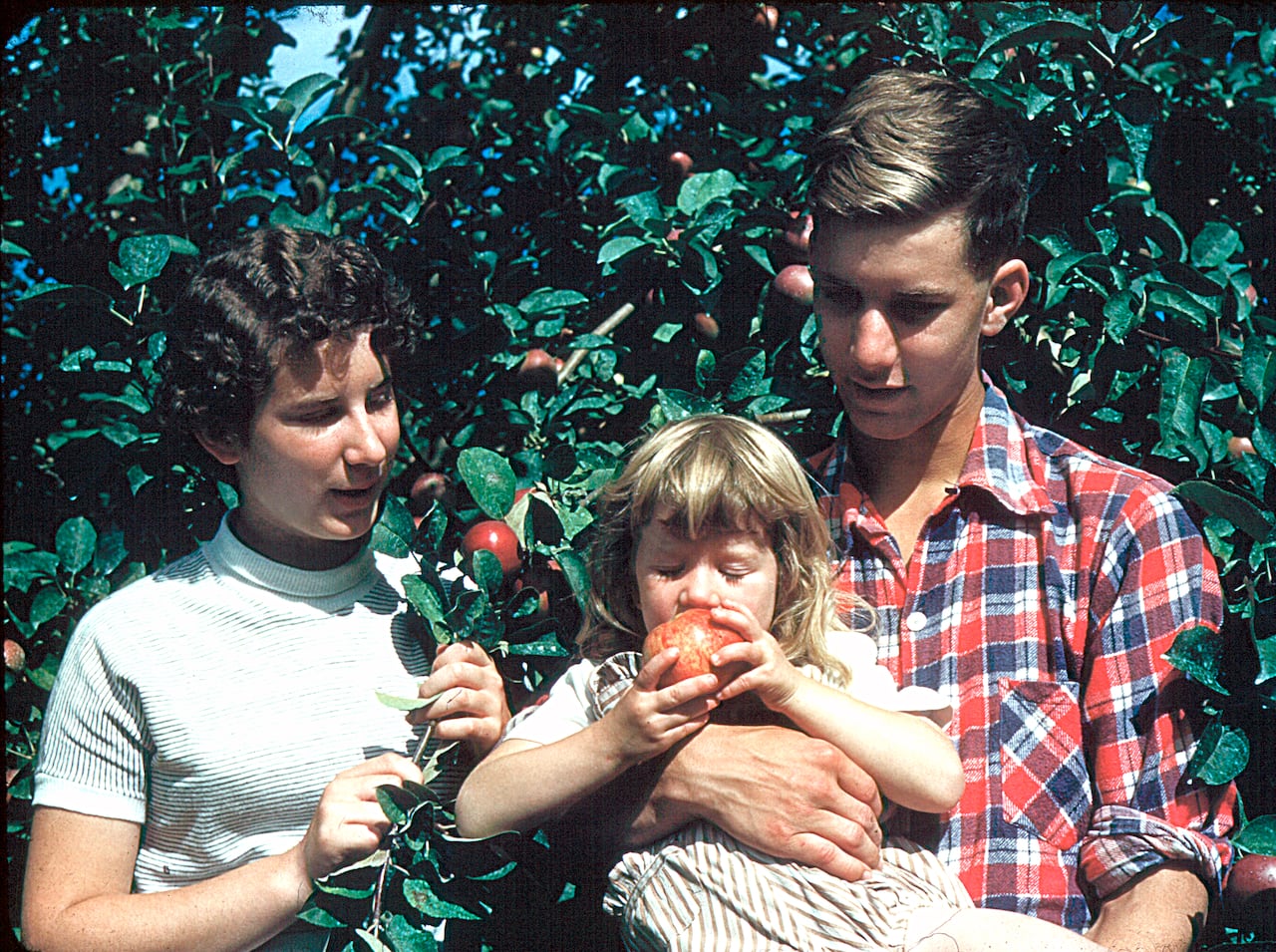 Two teenagers and a toddler stand near some trees
