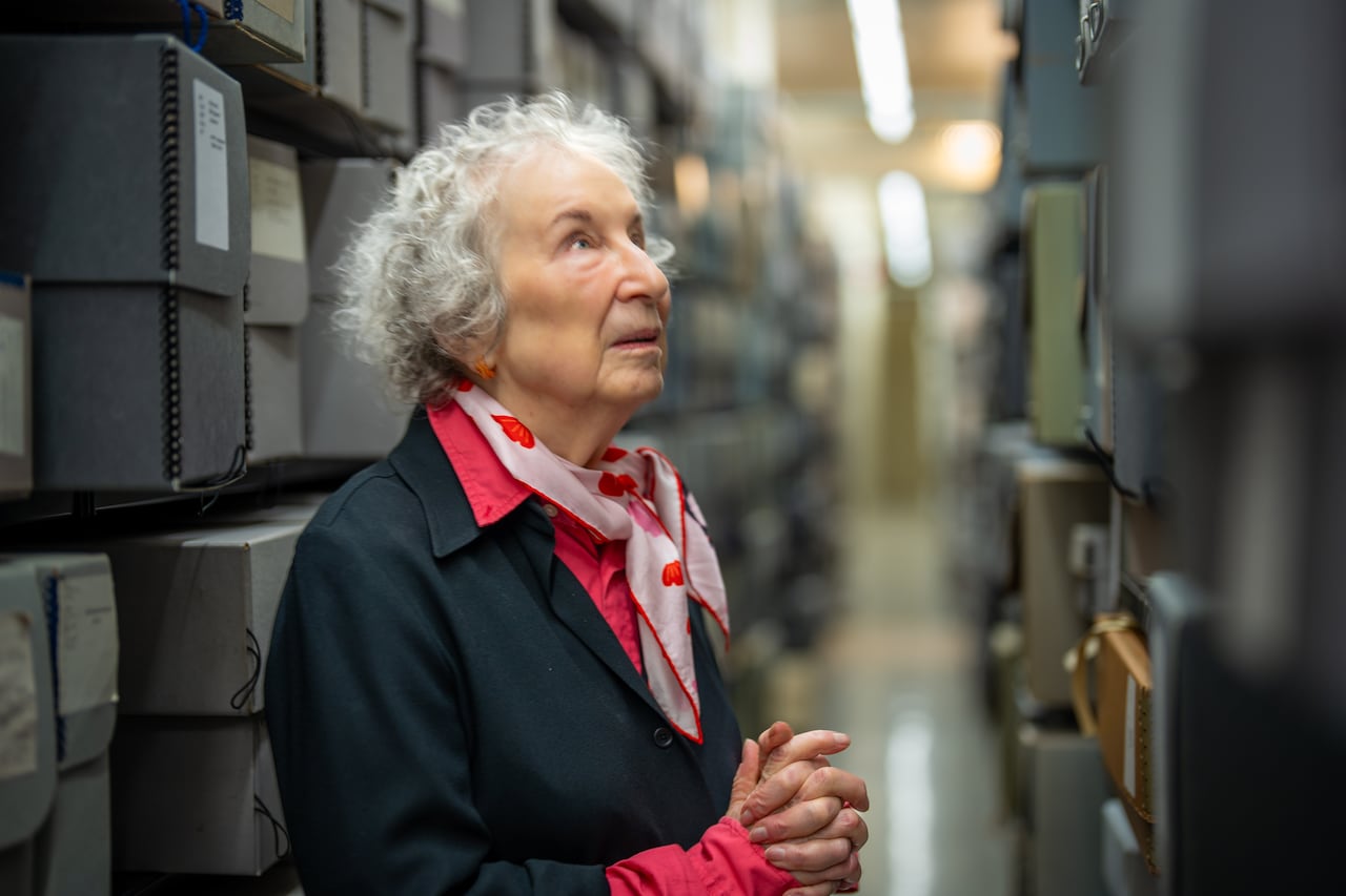 A woman standing in library stacks looks at books and papers on a shelf